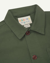 Front detail shot of  the neck and front buttons of a coriander green men's overshirt  showing the uskees brand  label