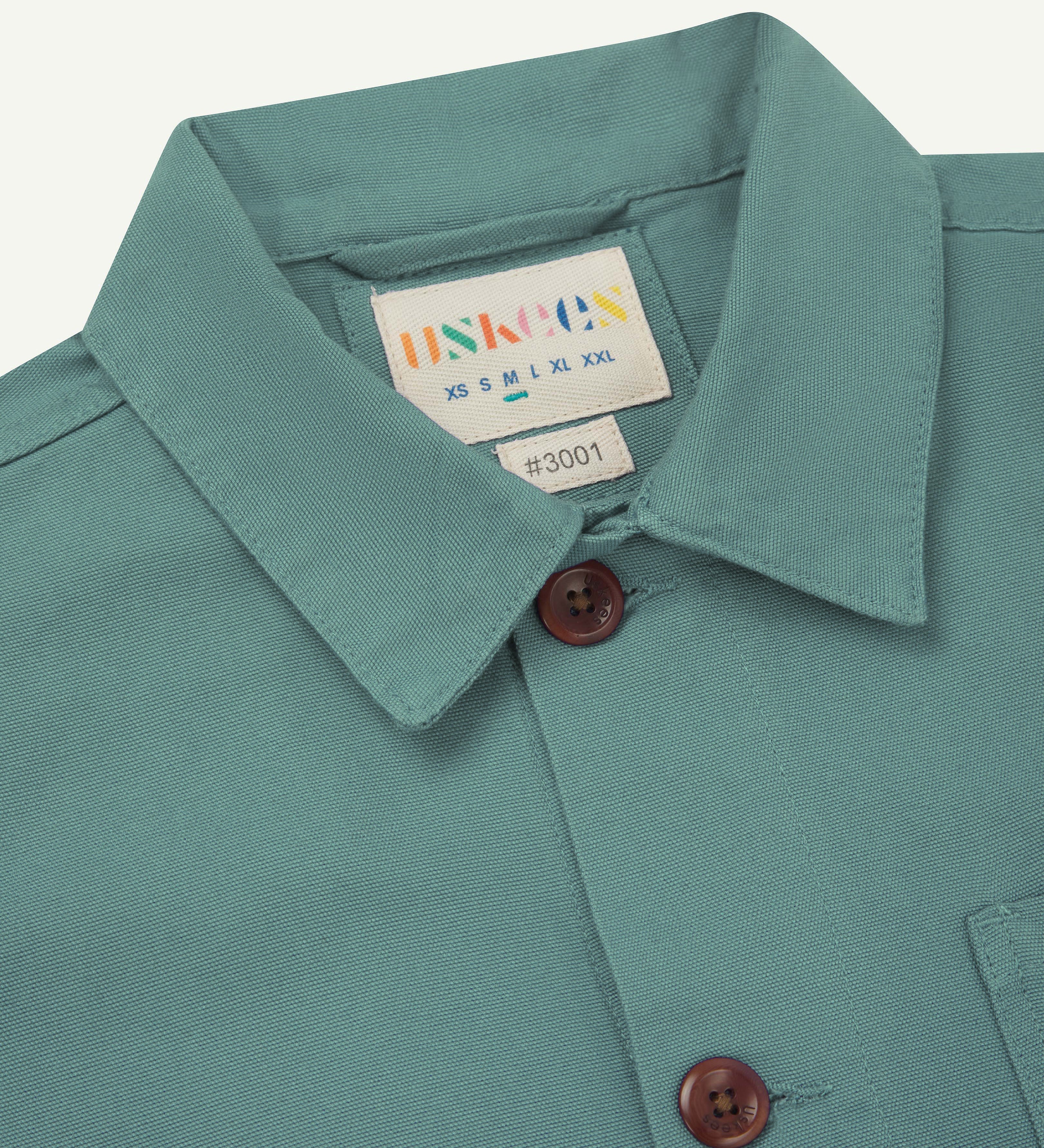 Front close up shot of an uskees eucalyptus green overshirt for men showing the brand label and corozo buttons