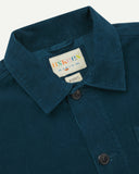 Close-up view of 3001 petrol blue, buttoned corduroy overshirt from Uskees showing corozo buttons, brand/size label, collar and hanging loop.