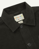 Close-up view of 3001 green-brown (seaweed), buttoned corduroy overshirt from Uskees showing corozo buttons, brand/size label, collar and hanging loop.