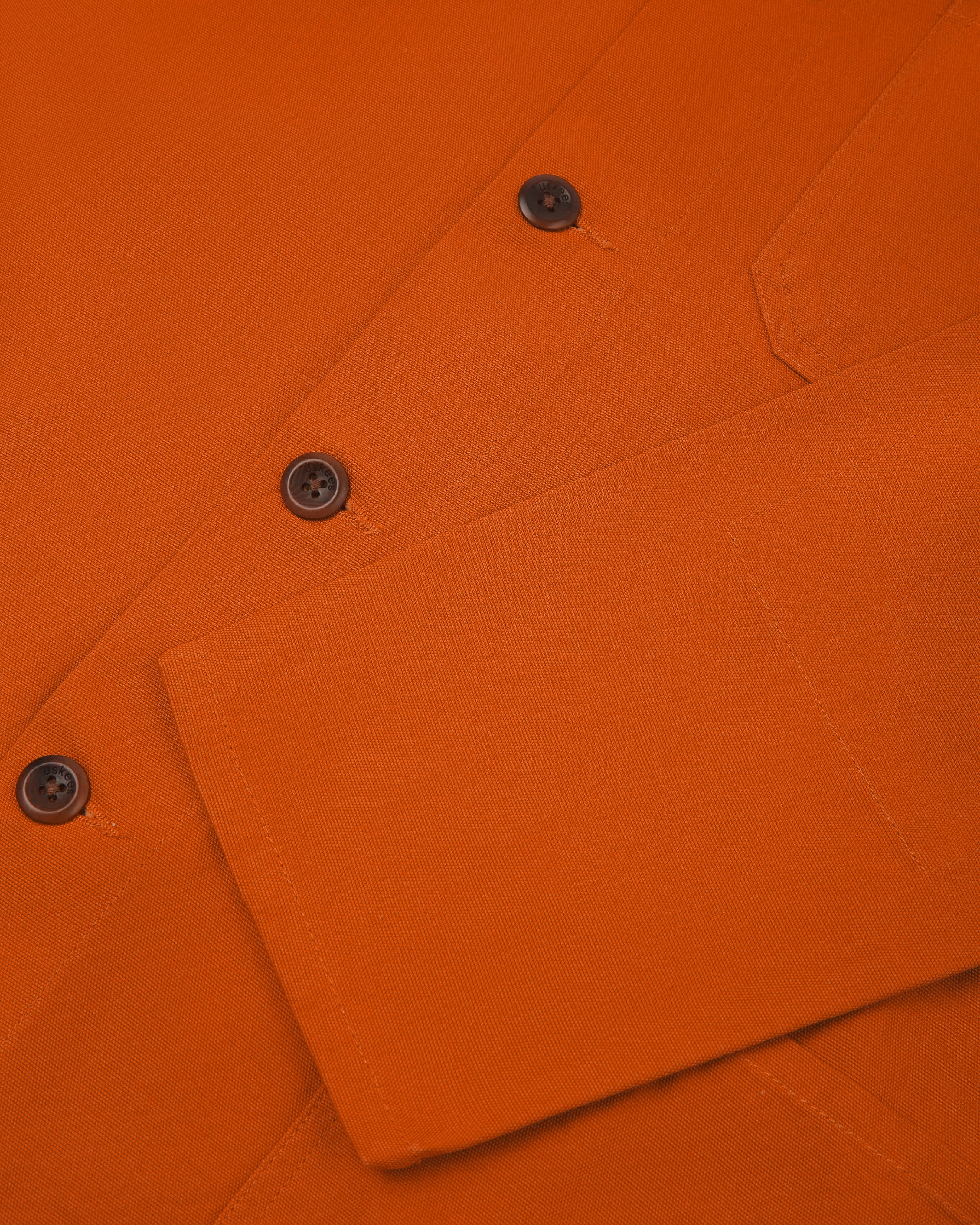 Front close shot of an uskees orange men's overshirt showing contrast brown corozo buttons and cuff/sleeve detail.