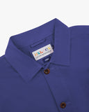Close-up view of 3001 ultra blue, buttoned organic cotton overshirt from Uskees showing corozo buttons, brand label, collar and hanging hoop.