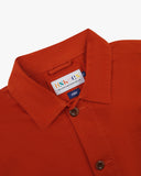 Close-up of an Uskees orange overshirt, showing the brand label at neck, on a white background