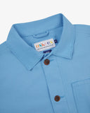 Close-up of an Uskees powder blue overshirt with a brand label on a white background