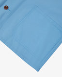 Close-up of an Uskees light blue overshirt pocket and brown Corozo button on a white background