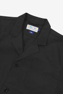 Angled top-half view of #3006, black organic cotton-twill blazer. With focus on collar, lapels, breast pocket, Uskees brand label and corozo buttons.
