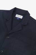 Angled top-half view of #3006, deep blue organic cotton-twill blazer. With focus on collar, lapels, breast pocket, Uskees brand label and corozo buttons.