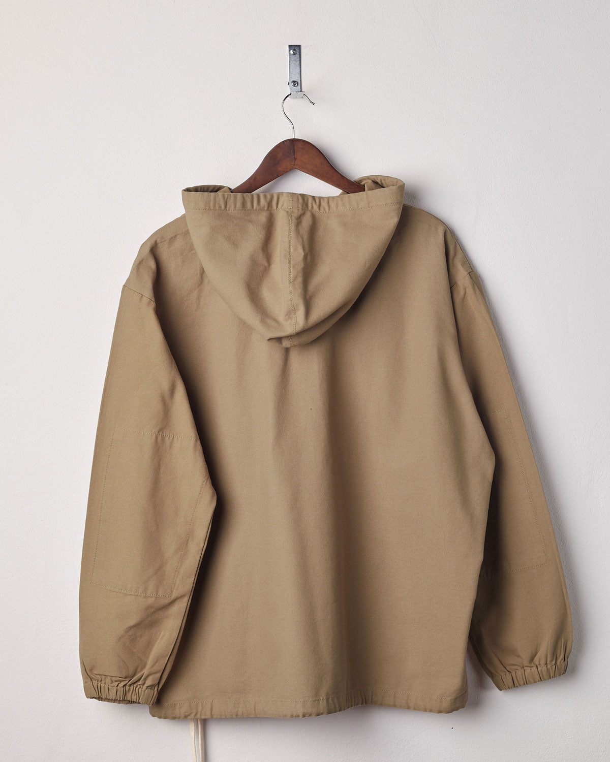 Back view of khaki coloured buttoned smock from Uskees with view of hood. Presented on hanger with white backdrop.