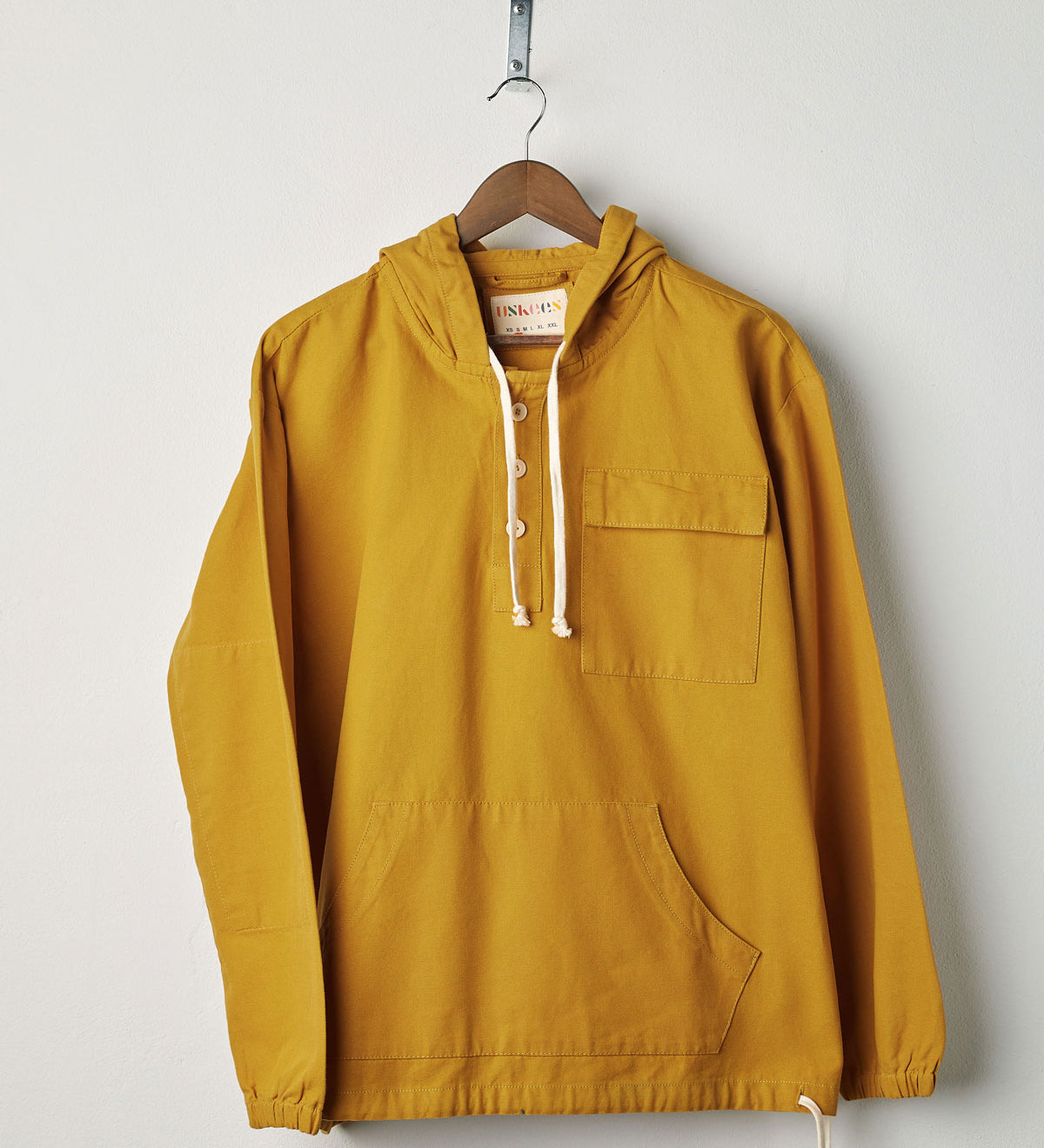 Front view of yellow coloured buttoned smock from Uskees with deep front pockets. Presented on hanger with white backdrop.