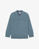Flat front view of knitted organic cotton blue-grey collared cardigan with 3 patch pockets from Uskees. Clearly showing corozo buttons, two branding labels and 3 pockets on the front.