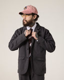 Bearded male model looking to his right wearing the Uskees charcoal docklands blazer, matching trousers and a white shirt. Can see tattoos on his hands.