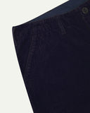 Close-up front view of left front pocket, belt loops, triple stitching, Corozo button and contrasting coloured lining material of midnight blue corduroy pants.