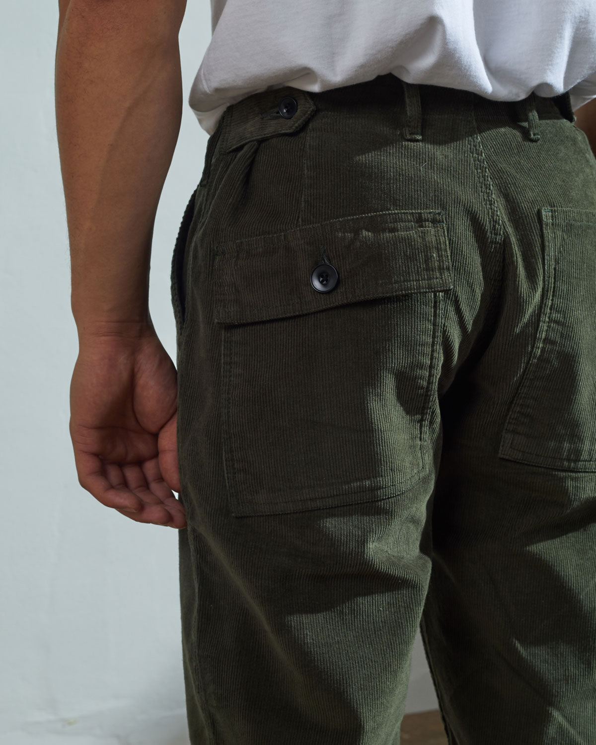 Close-up view of Uskees vine green corduroy work pants with focus on natural corozo buttons, left rear pocket, belt loops, triple stitching and adjustable button waist.