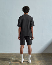 Full-length back view of model wearing faded black, relaxed cut organic cotton #7008 oversized jersey T-shirt by Uskees paired with matching shorts.