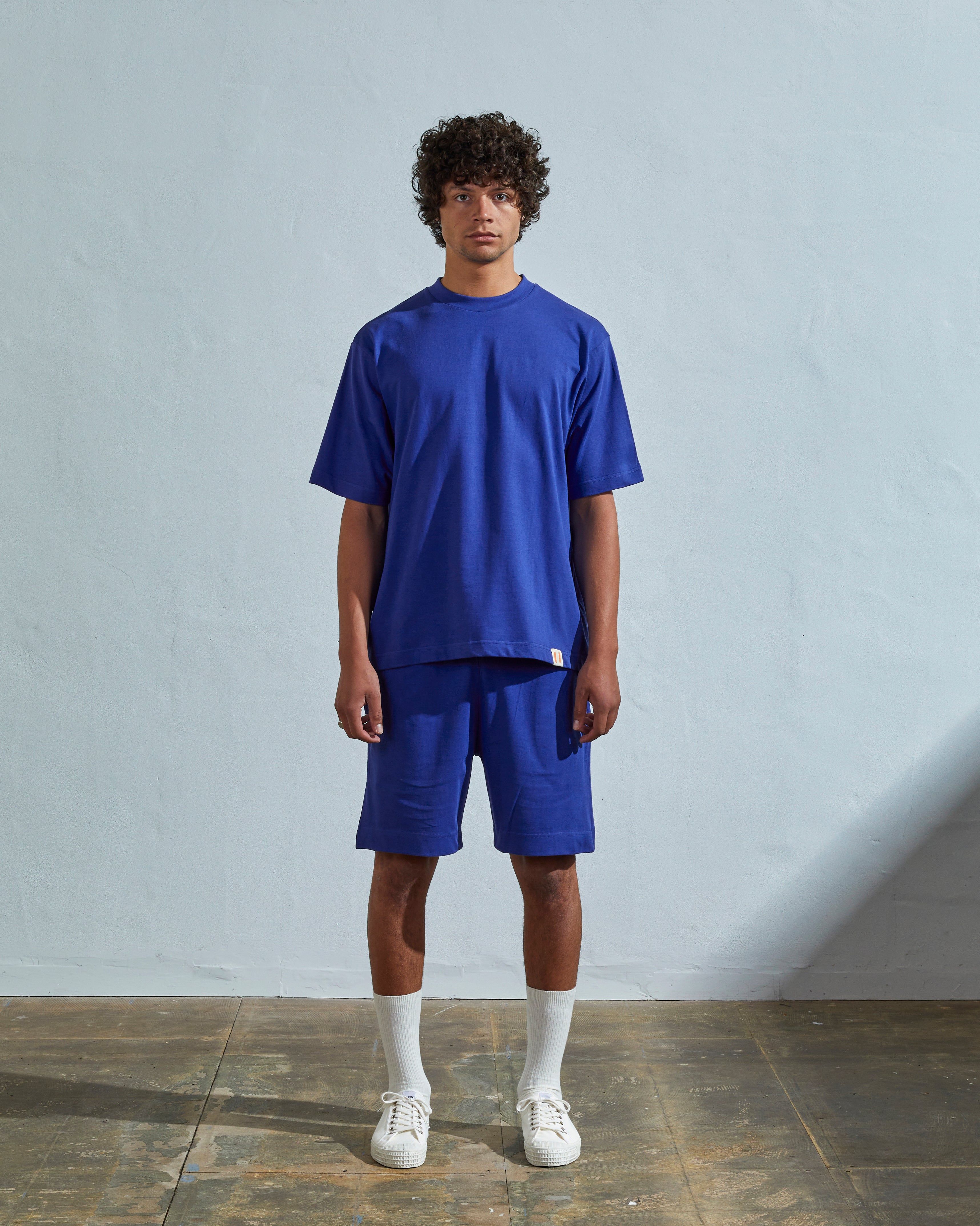 Full-length front view of model wearing striking ultra blue organic cotton #7008 oversized jersey T-shirt by Uskees paired with matching shorts.