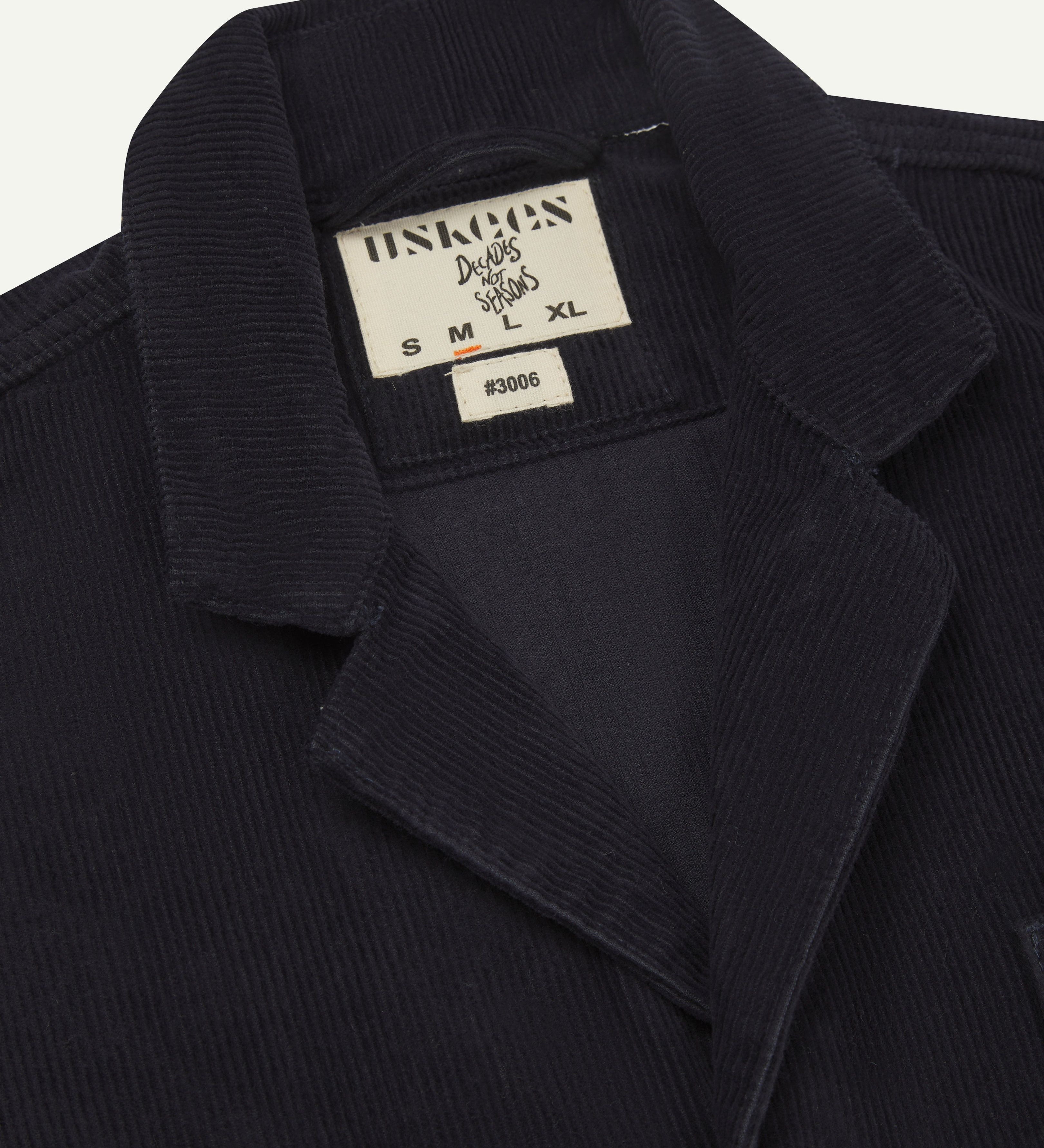 Close-up front view of men's corduroy dark blue blazer with 3 patch pockets from Uskees showing the collar, lapels and brand label.
