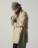 Male model wearing a beige Uskees car coat and green knit beanie against a plain background