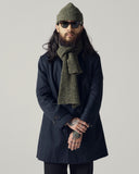 Male model wearing an Uskees dark blue car coat, green beanie, and scarf against a plain background