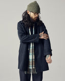 Man wearing an Uskees dark blue car coat, green beanie, and plaid scarf on a plain background