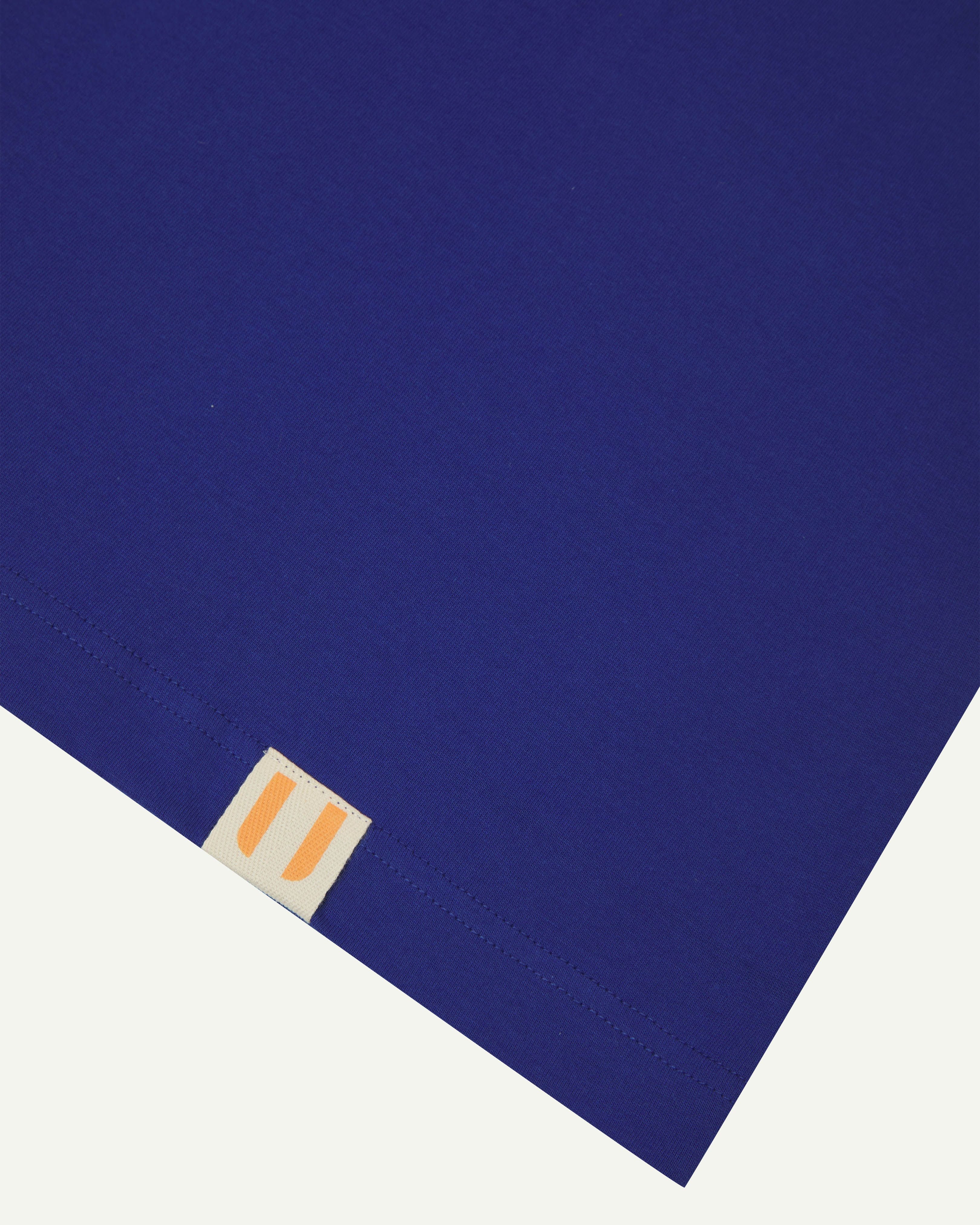 Close up view of ultra blue organic cotton #7008 oversized T-shirt by Uskees showing hem detail with uskees logo label.