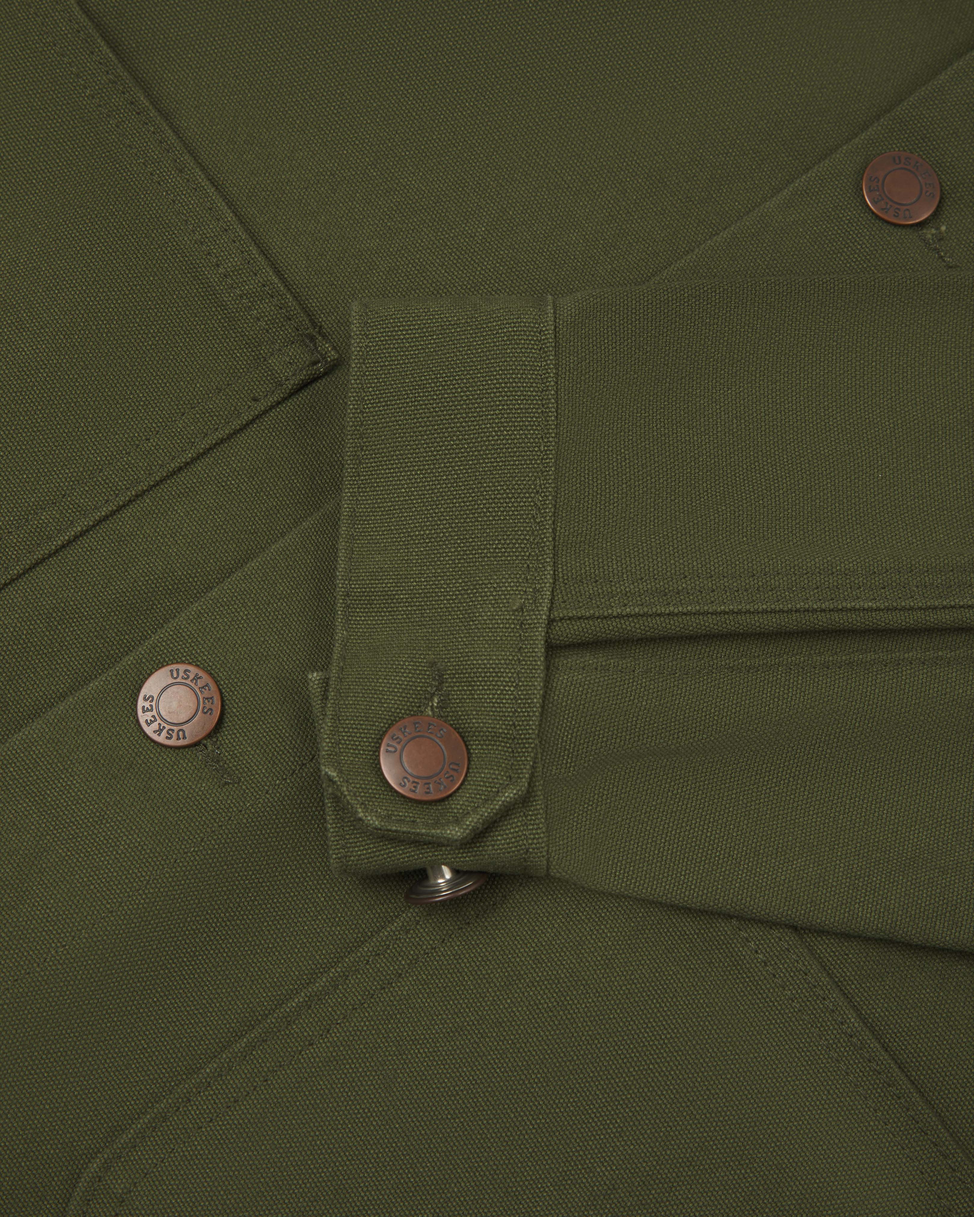 Close-up view of uskees cotton canvas chore jacket in coriander green  showing the adjuster buttons on the cuffs