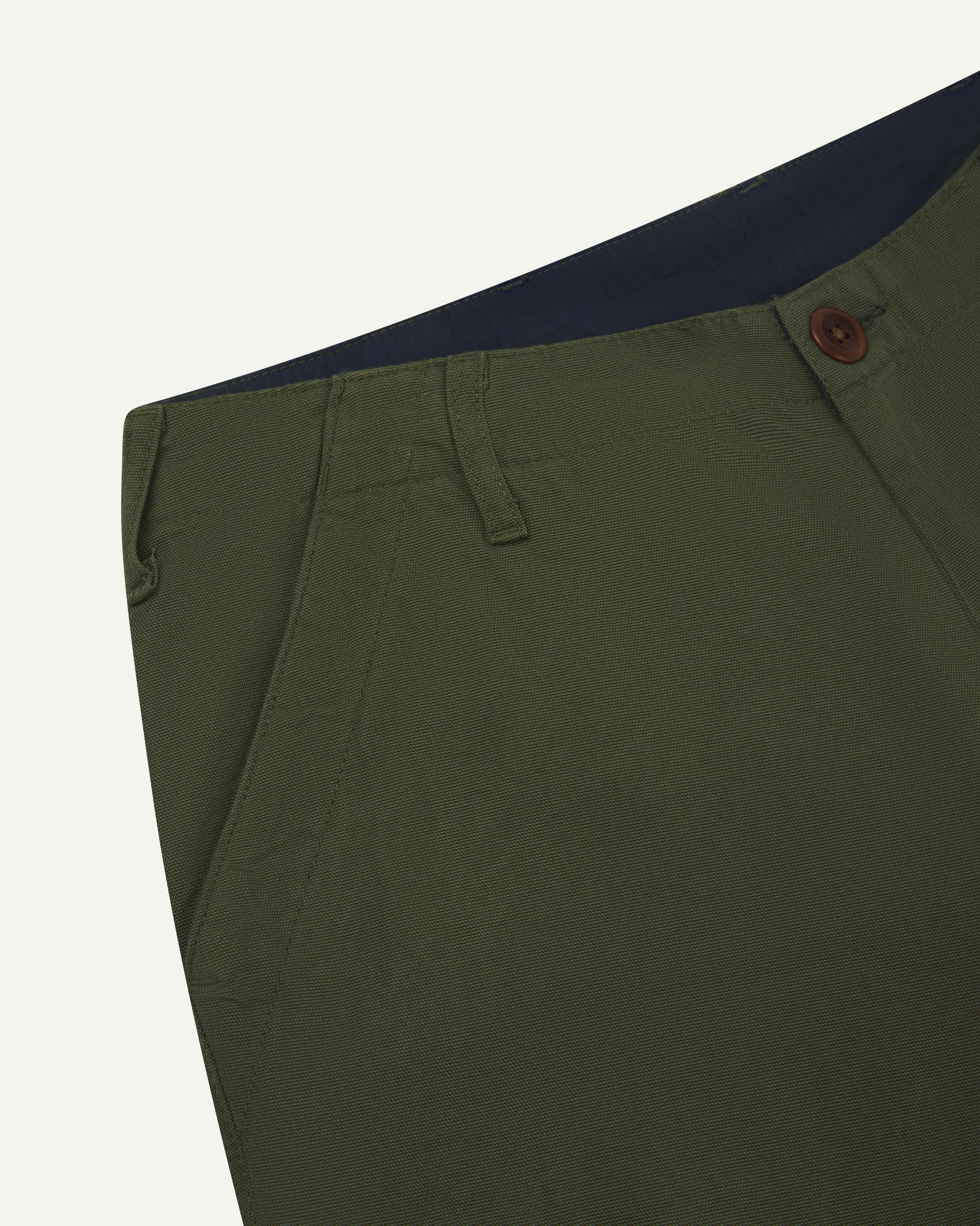 Close up shot of front waistband of the Uskees #5005 workwear pants in 'coriander' green showing Corozo button, belt loops and pockets.