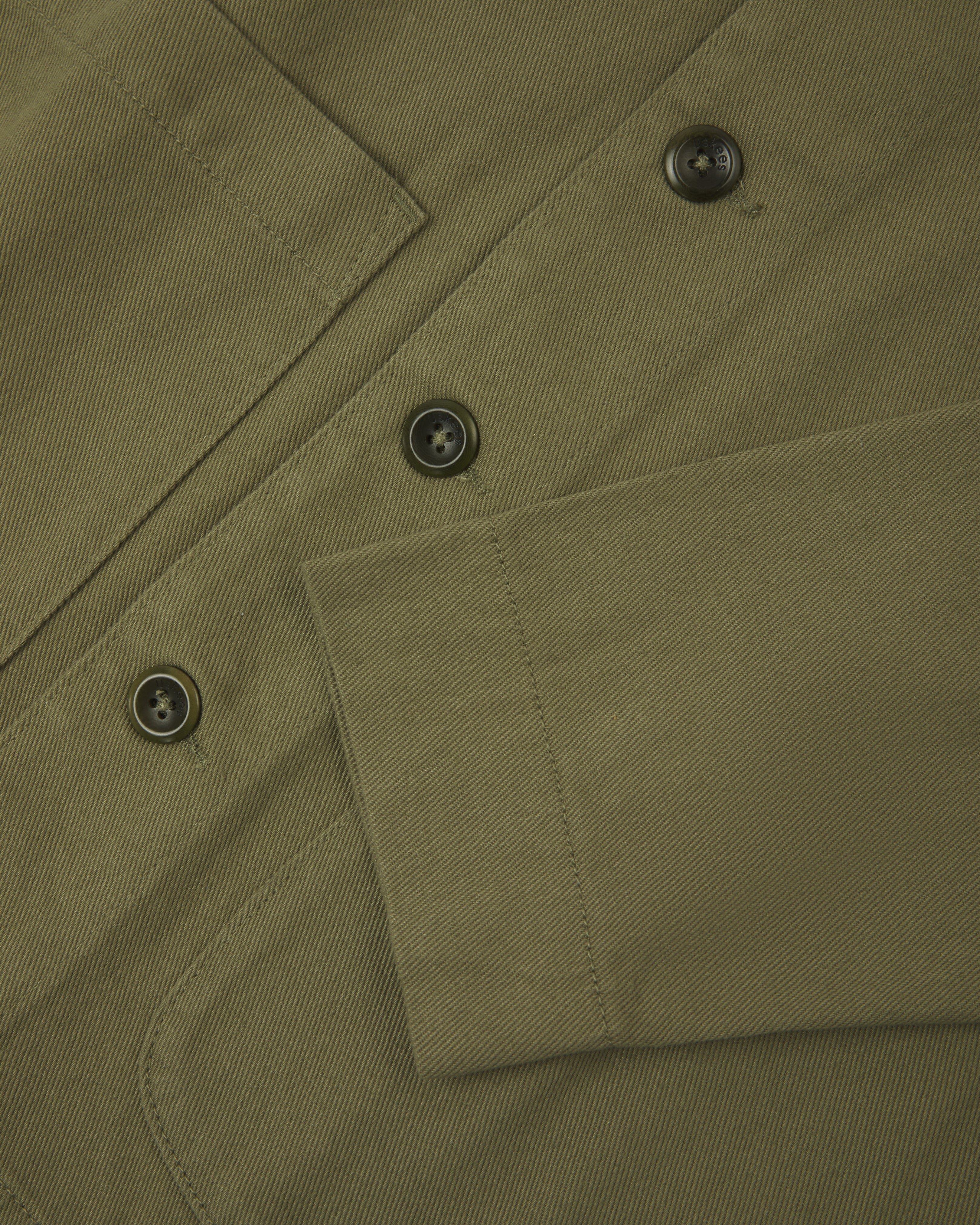 Front close view of moss green organic cotton drill commuter blazer showing cuff/sleeve, corozo buttons &  patch pocket