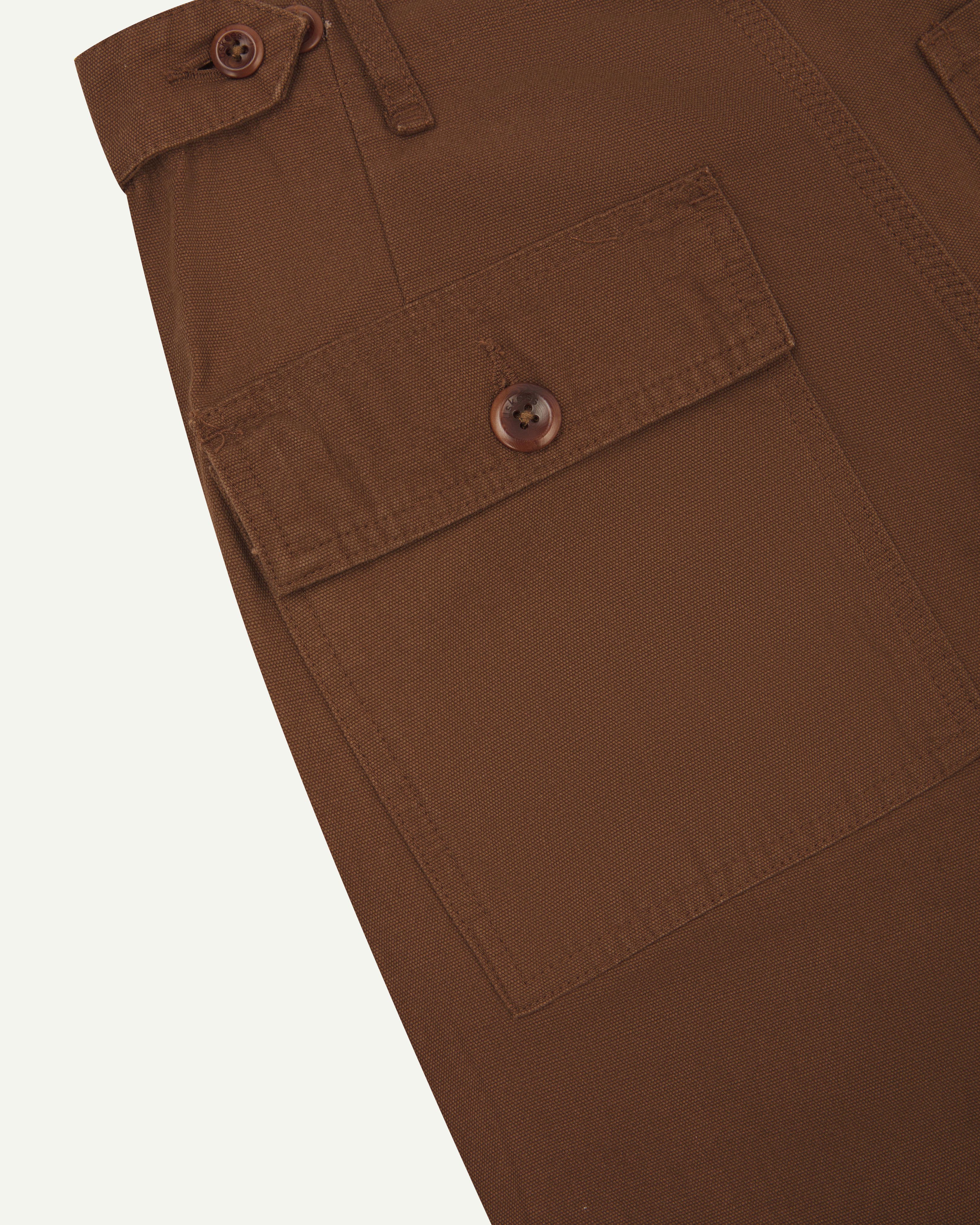 Close-up angled view of Uskees chocolate coloured cotton work pants with focus on natural corozo buttons, left rear pocket, belt loops, triple stitching and adjustable button waist