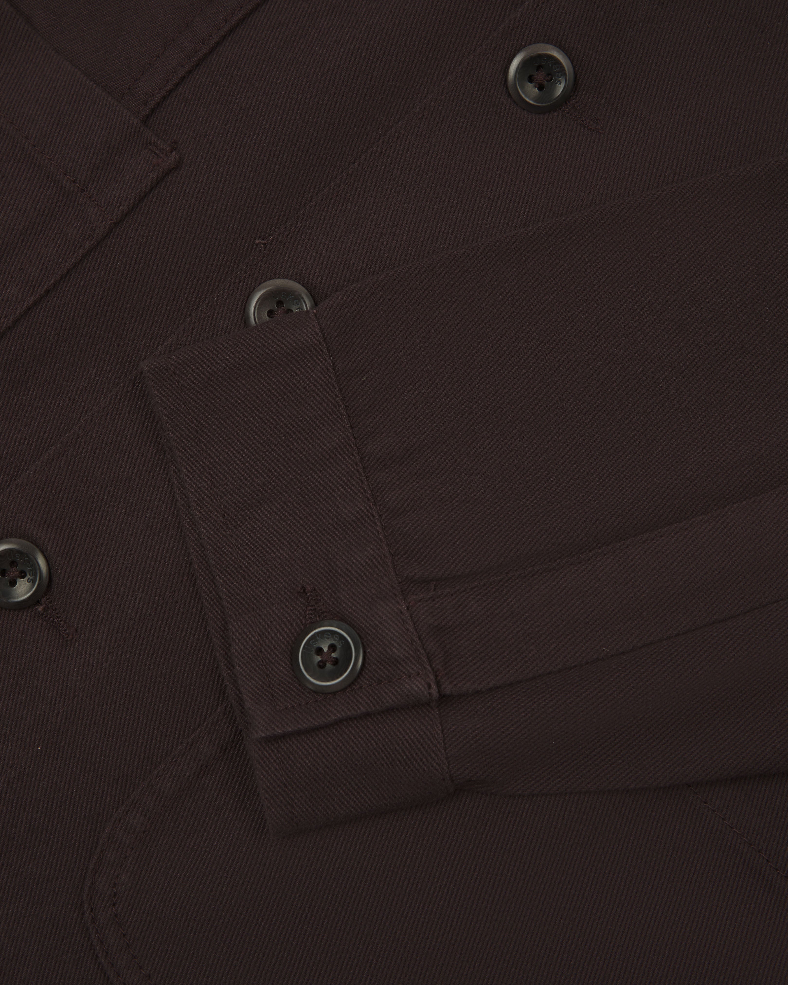 Close-up view of uskees cotton drill overshirt showing front pockets, corozo buttons and sleeve/cuff detail.