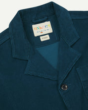 Close-up front view of men's corduroy petrol blue blazer from Uskees showing the collar, lapels and brand label.
