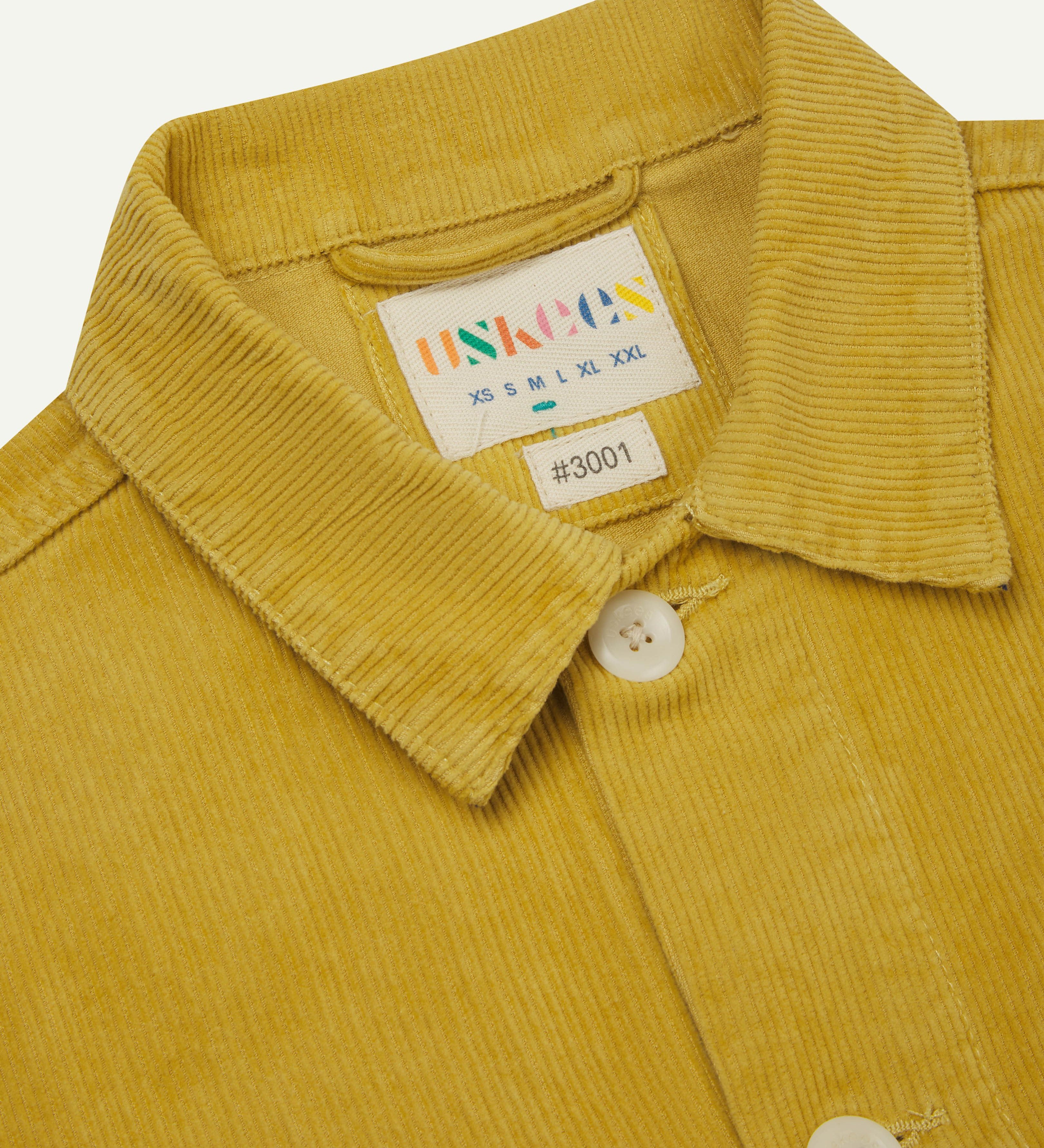 front close shot of acid yellow coloured, buttoned corduroy overshirt from Uskees. Clear view of corozo buttons and inner neck brand label