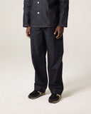 Model wearing Uskees raw orta denim workwear pants in dark indigo with matching overshirt.