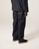 Back view of male model wearing Uskees raw orta denim workwear pants in dark indigo with matching overshirt.