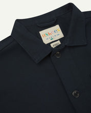 Front close-up shot of dark blue buttoned organic cotton-drill overshirt from Uskees. Showing the collar and brand/size label.