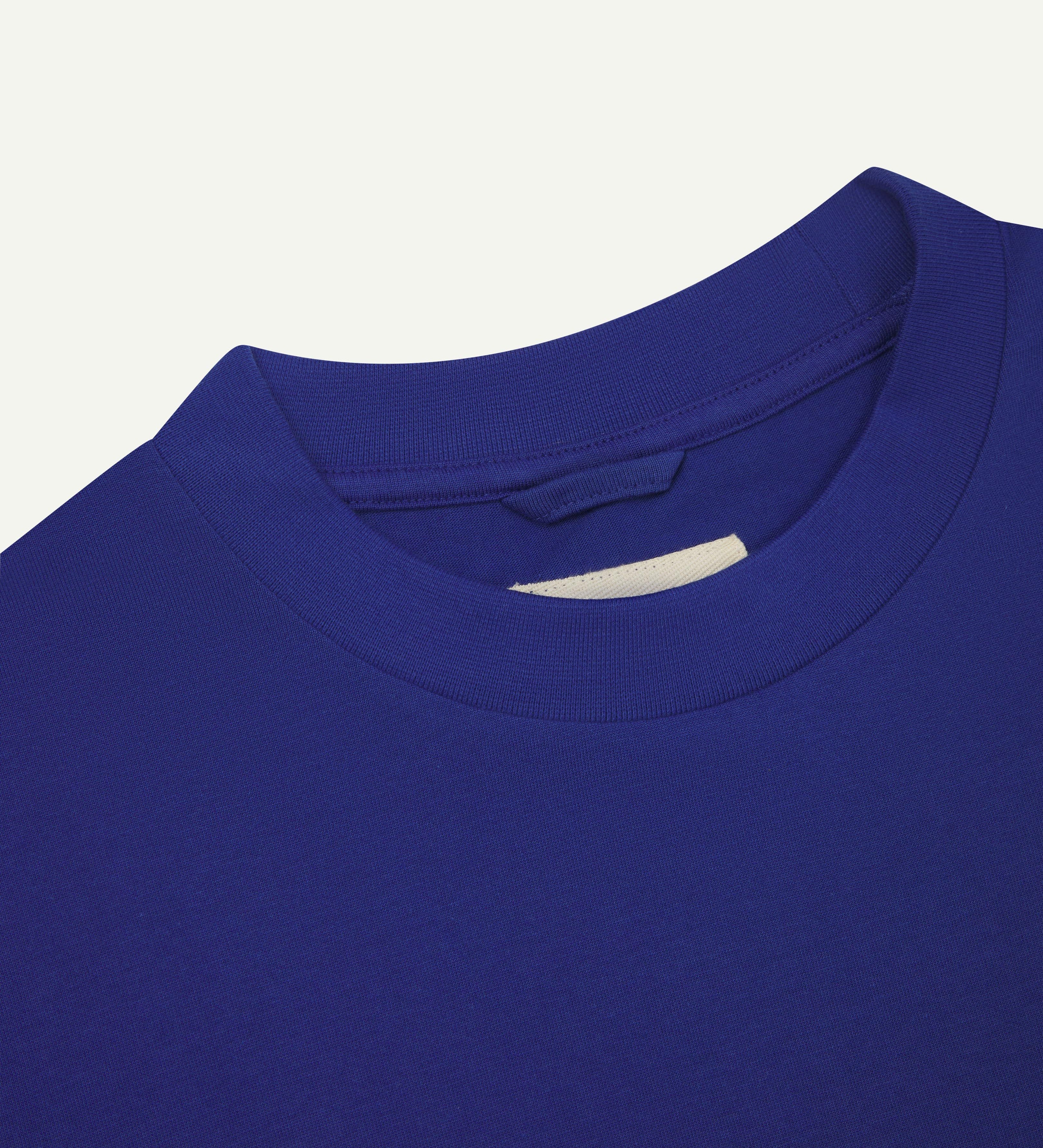Front close view of  neck label  of ultra blue organic cotton #7008 oversized T-shirt by Uskees against white background.