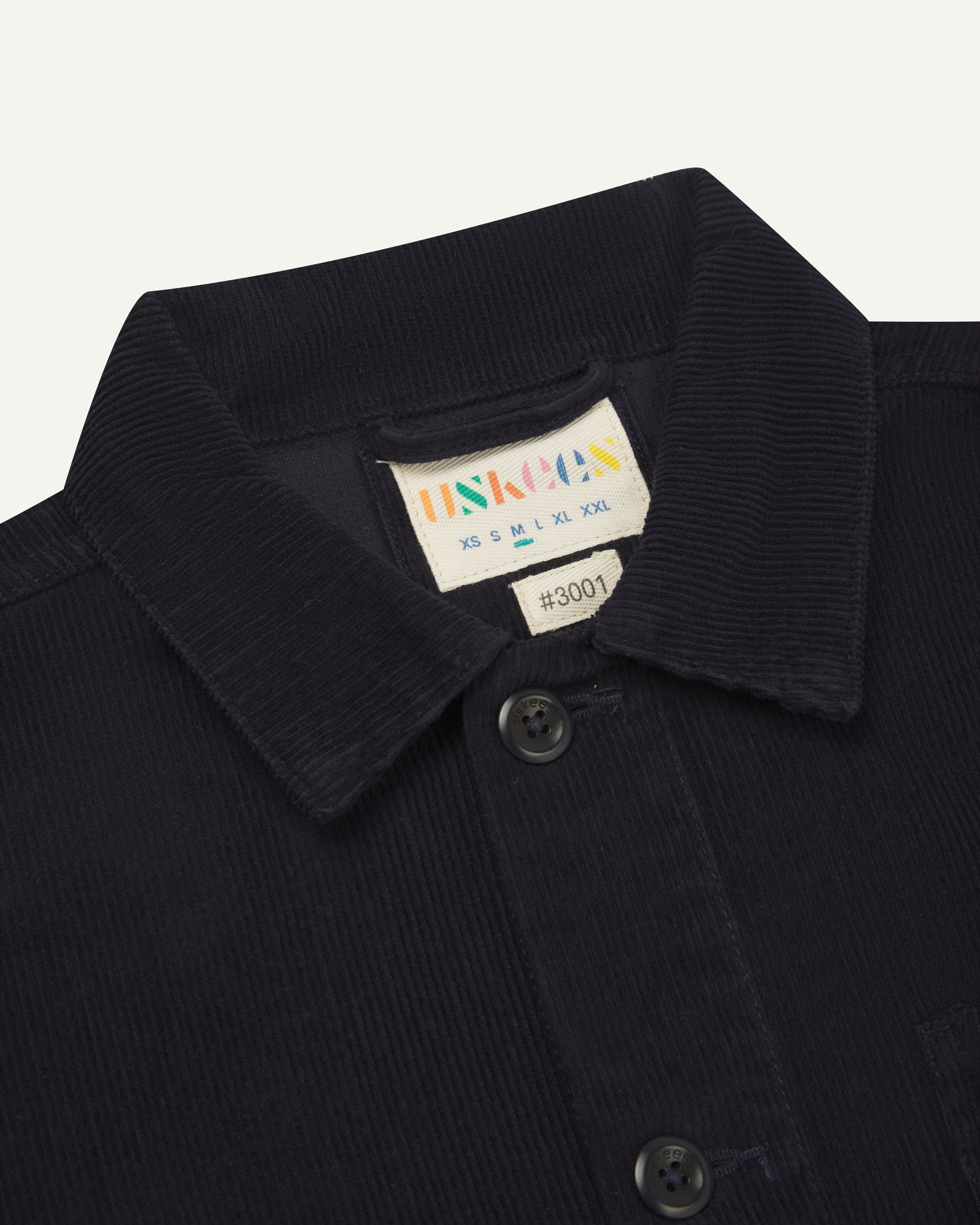 Close up front shot of Uskees dark blue corduroy 3001 over-shirt  showing collar and inner brand label