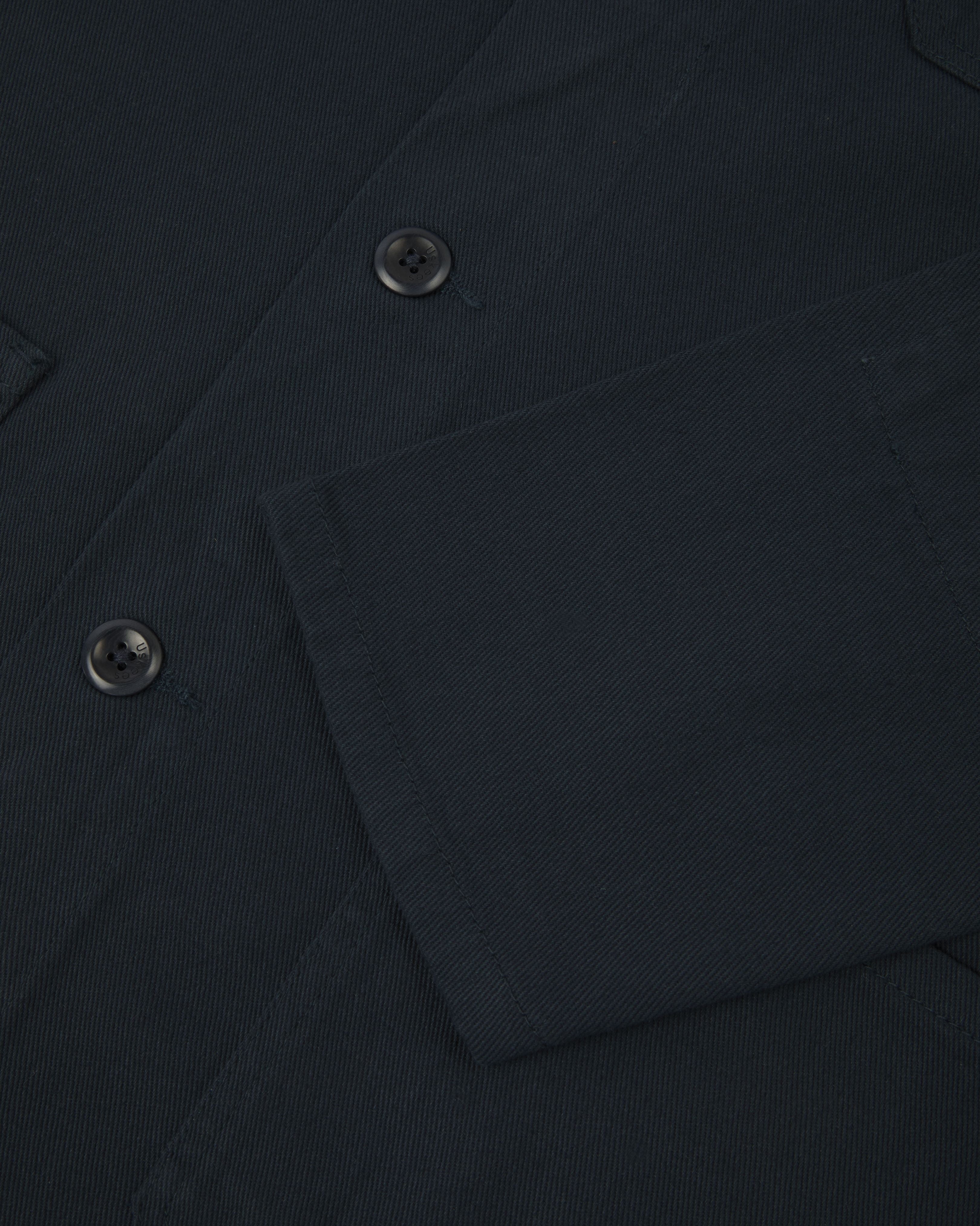 Detail shot of dark-blue buttoned organic cotton-drill shirt/jacket from Uskees. Showing sleeve and blue corozo buttons.
