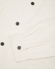 Close-up view of Uskees cream organic cotton coach jacket showing contrast black poppers on front and cuff