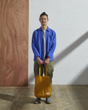 Full-length, front-view of model carrying Uskees #4002, small yellow tote bag. Paired with #3002, blue zip-front jacket.