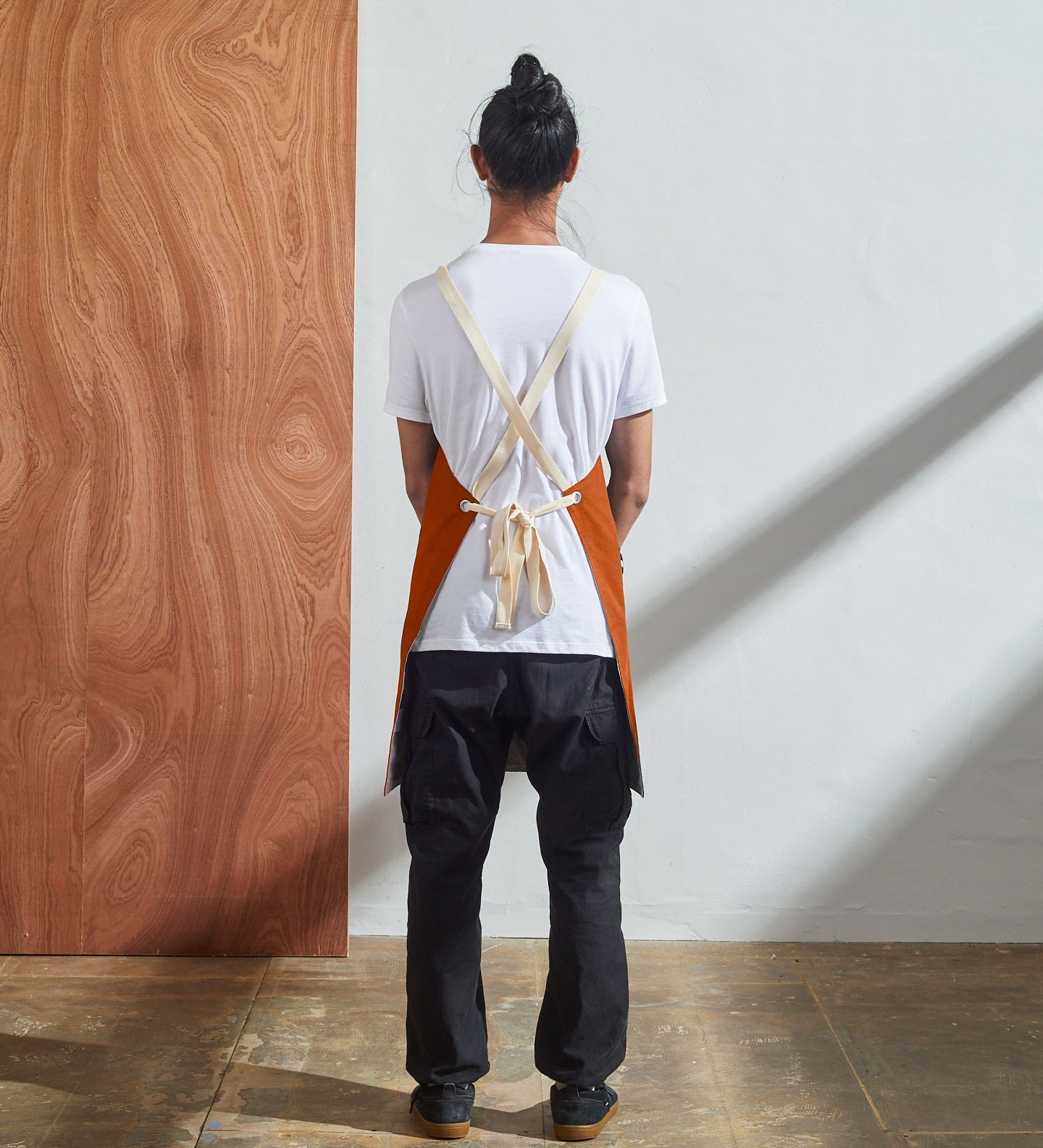 Full-length, rear view of model wearing Uskees #9001 gold work apron by Uskees. Clear view of cream rear ties.