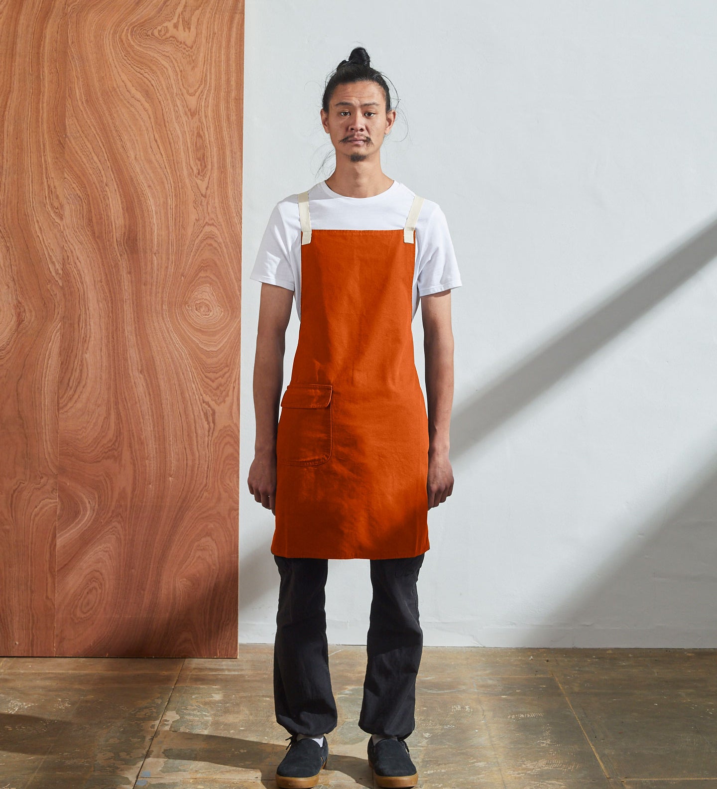 Full-length, front view of male model wearing Uskees #9001 gold work apron by Uskees. Showing convenient hip pocket and contrasting cream straps.