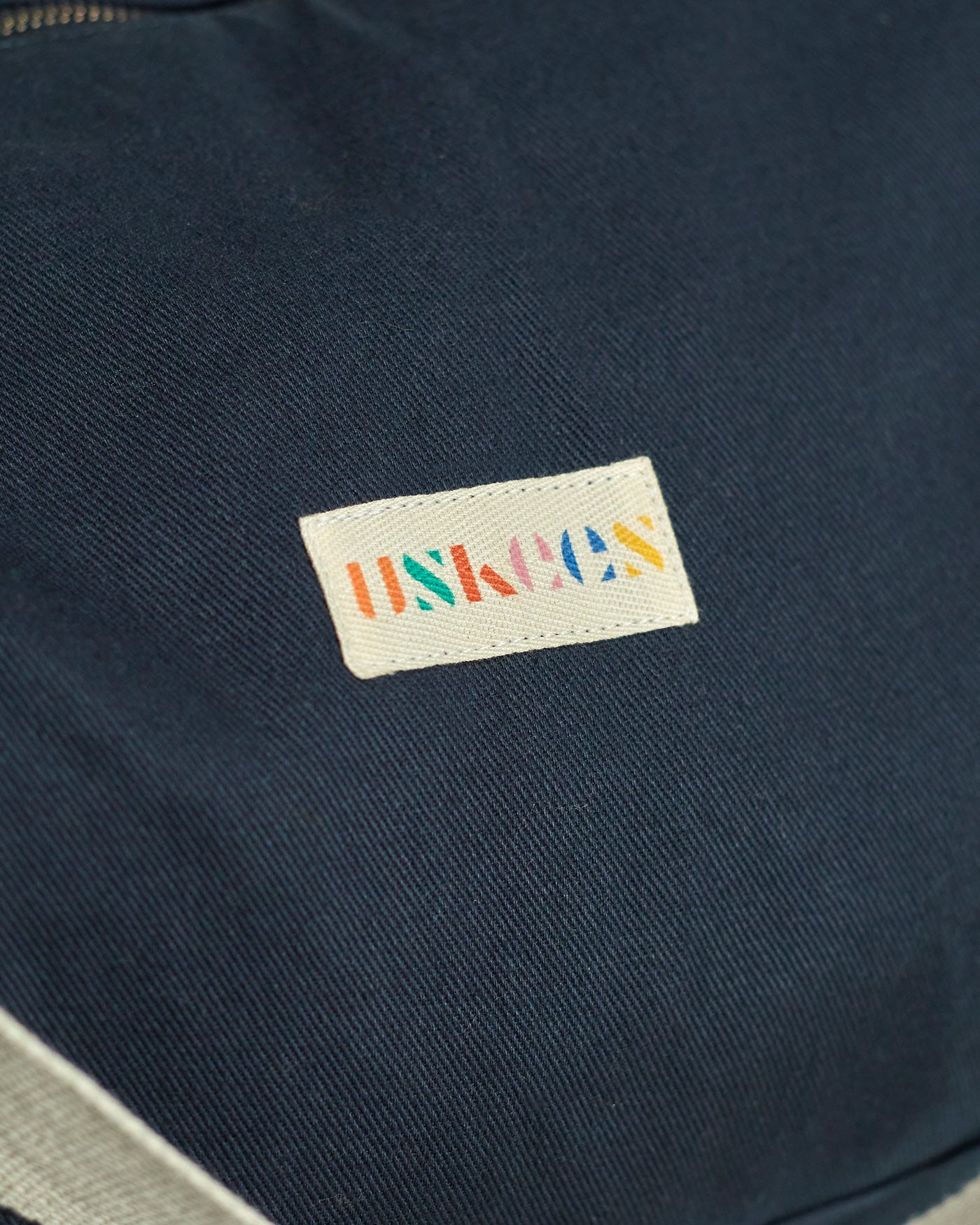 Close-up view of Uskees logo and zipper of the #0403 barrel bag in blueberry.