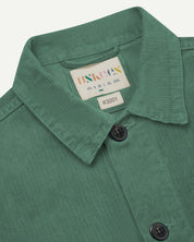 Close-up view of #3001 light green, buttoned corduroy overshirt from Uskees. Clear view of cream corozo buttons, brand/size label and collar.