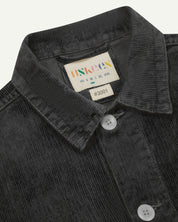 Close-up view of dark grey, buttoned corduroy overshirt from Uskees. Clear view of corozo buttons, uskees brand label and collar.