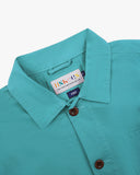 Close-up view of 3001 aqua-blue, buttoned organic cotton overshirt from Uskees showing corozo buttons, brand label, collar and hanging hoop.
