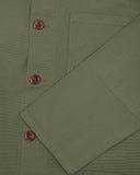 Closer view of mid section of army green, buttoned organic cotton overshirt from Uskees. Focus on cuff, pockets and corozo buttons.