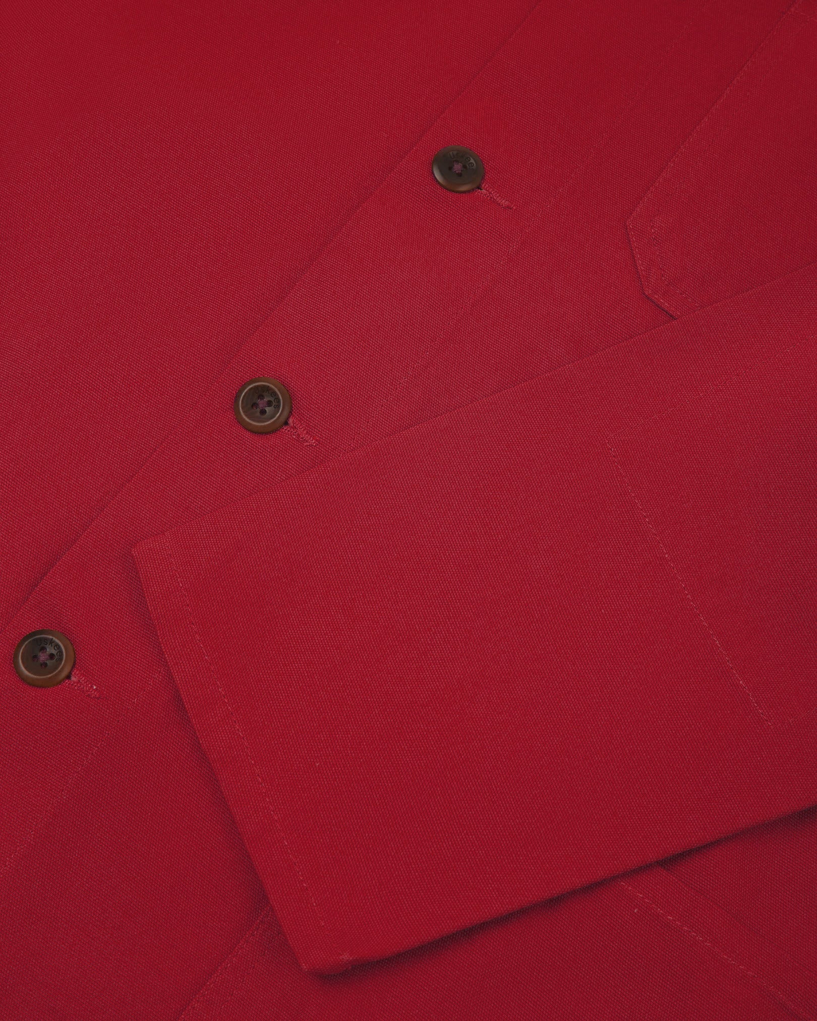 Closer view of mid section of berry red, buttoned organic cotton overshirt from Uskees. Focus on cuff, placket and corozo buttons.