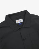 Close-up view of 3001 black, buttoned ripstop overshirt from Uskees showing corozo buttons, brand label, collar and hanging hoop.