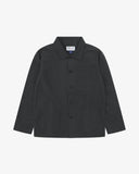 Front flat shot of black, buttoned ripstop overshirt. Clear view of chest and hip pockets, corozo buttons and Uskees branding label.