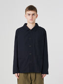 Top-half view of man wearing an Uskees black ripstop overshirt indicating roomy, boxy fit with clear view of deep pockets on the chest and front.